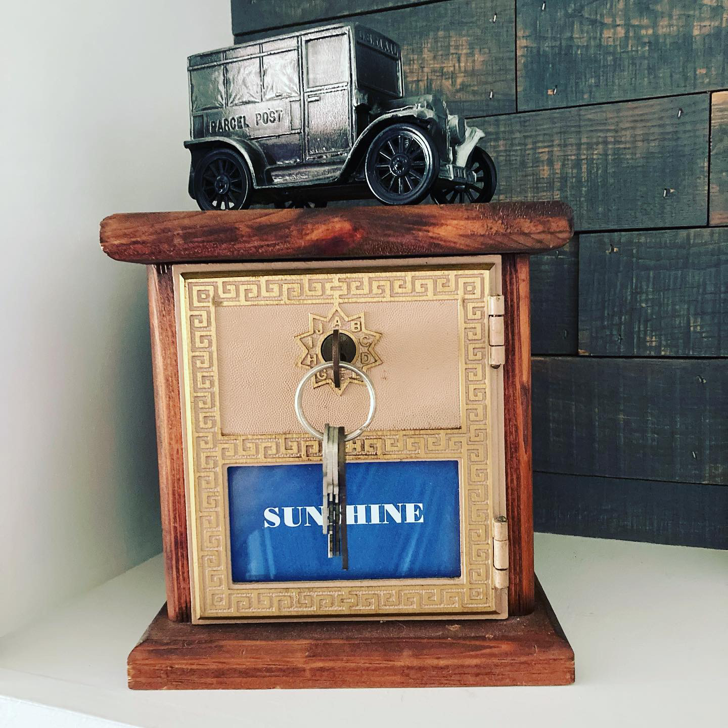 Coin bank made from wood and an old post office box with key in the lock; a metal model mail truck sits on top