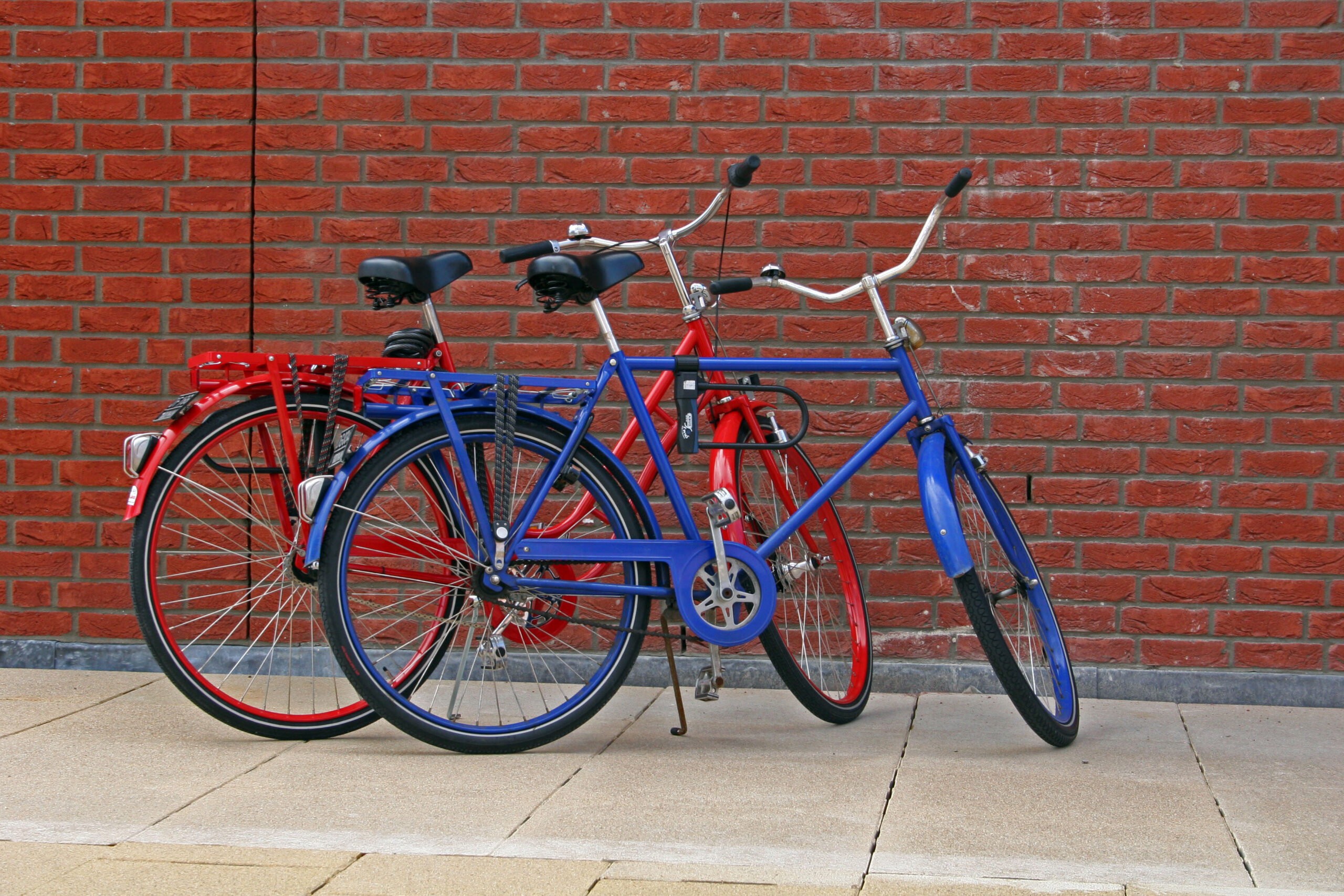 Red and blue bikes in front of a wall of bricks.